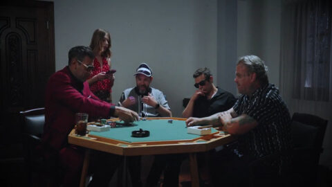 Young woman in a modest dress standing nervously in a dimly lit room with a poker table visible in the background, cards and chips scattered across felt, three silhouetted men seated, her expression caught between resignation and determination as she faces the debt her father accumulated
